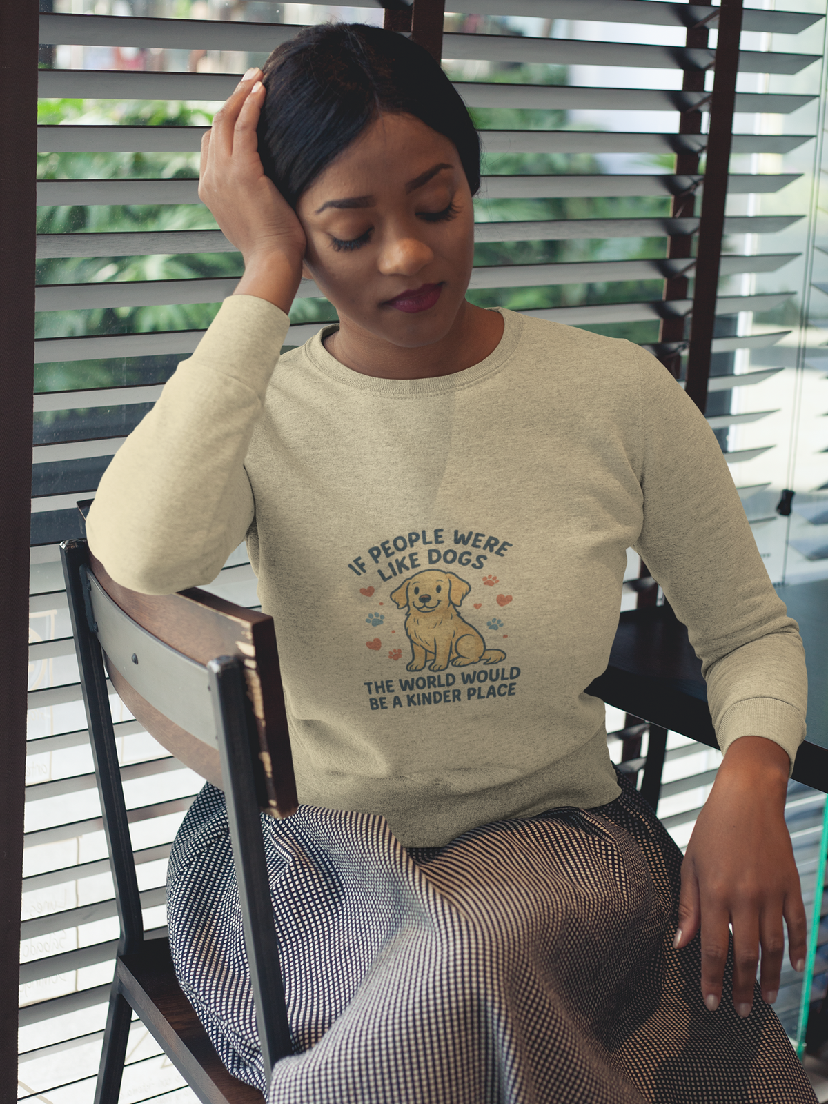 Seated woman wearing a cream sweatshirt with a dog illustration and “If people were like dogs, the world would be a kinder place.”